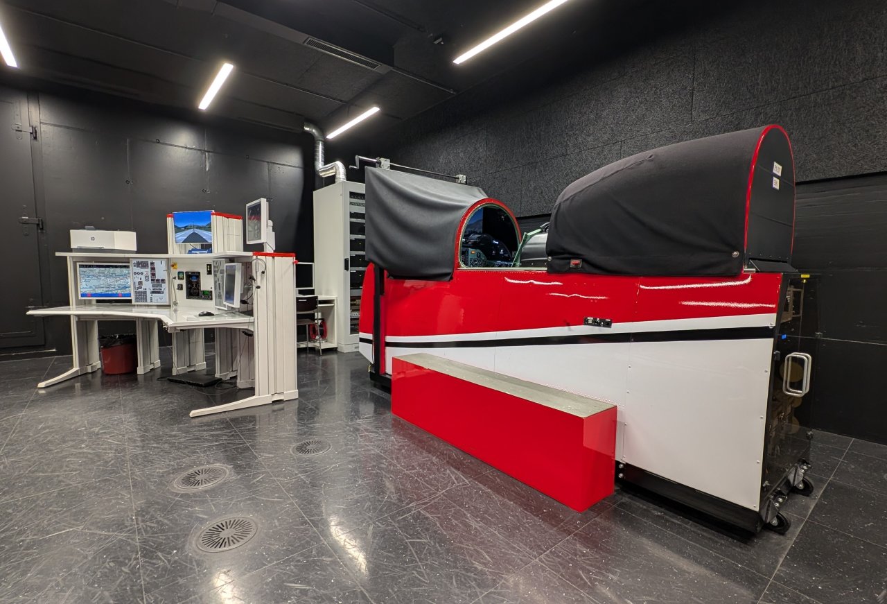 PC-7-Simulator steht in einem Raum. Links davon steht ein Tisch mit elektronischen Geräten darauf.
